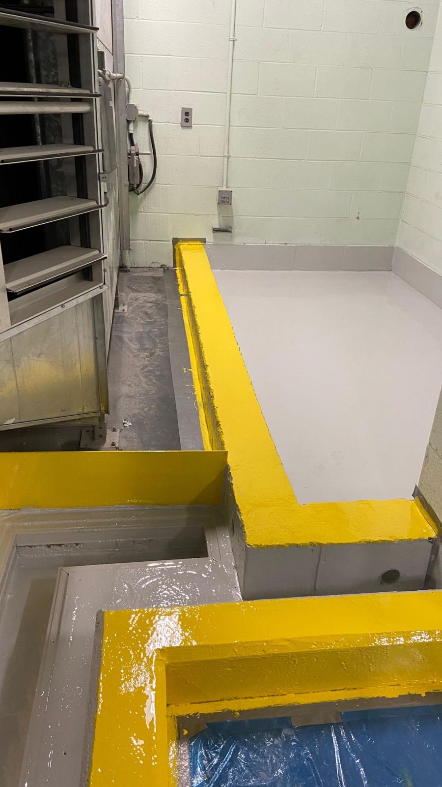 Yellow coated containment curb beside grey epoxy floor